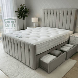 The Sparrow divan bed in a soft grey fabric, shown with two large side drawers pulled out and filled with neatly folded cushions and bedding.